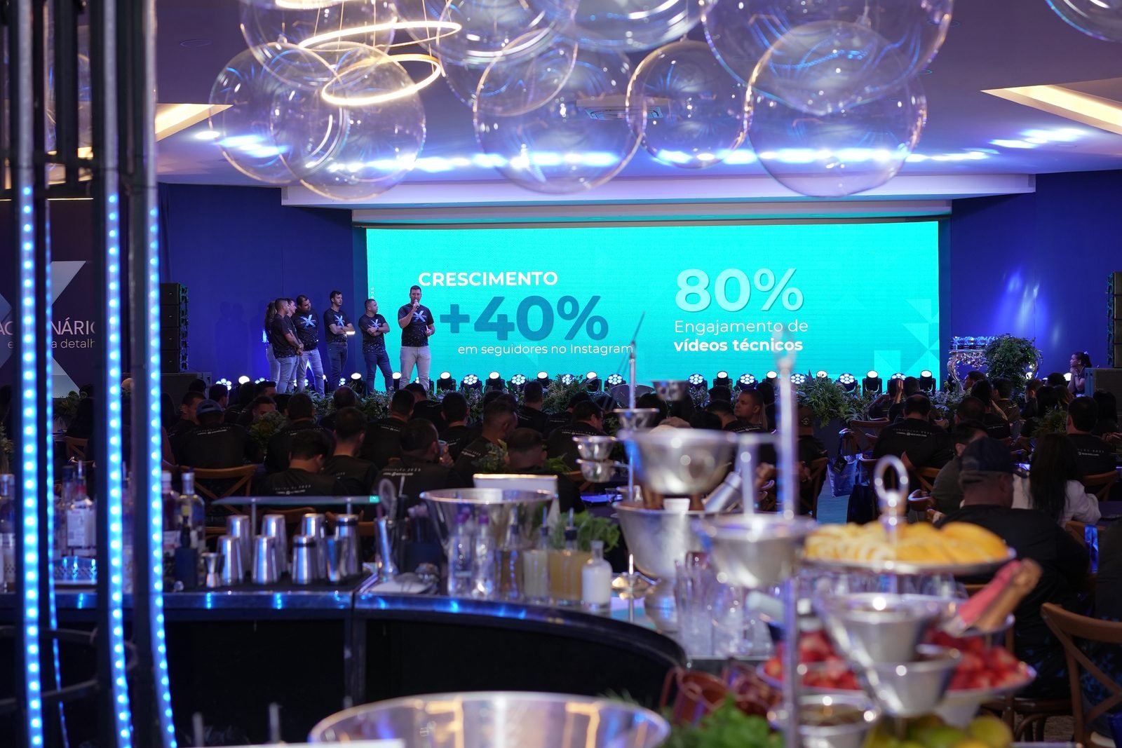 Vista ampla do salão — gaiola de luz LED, bar gastronômico e painel LED